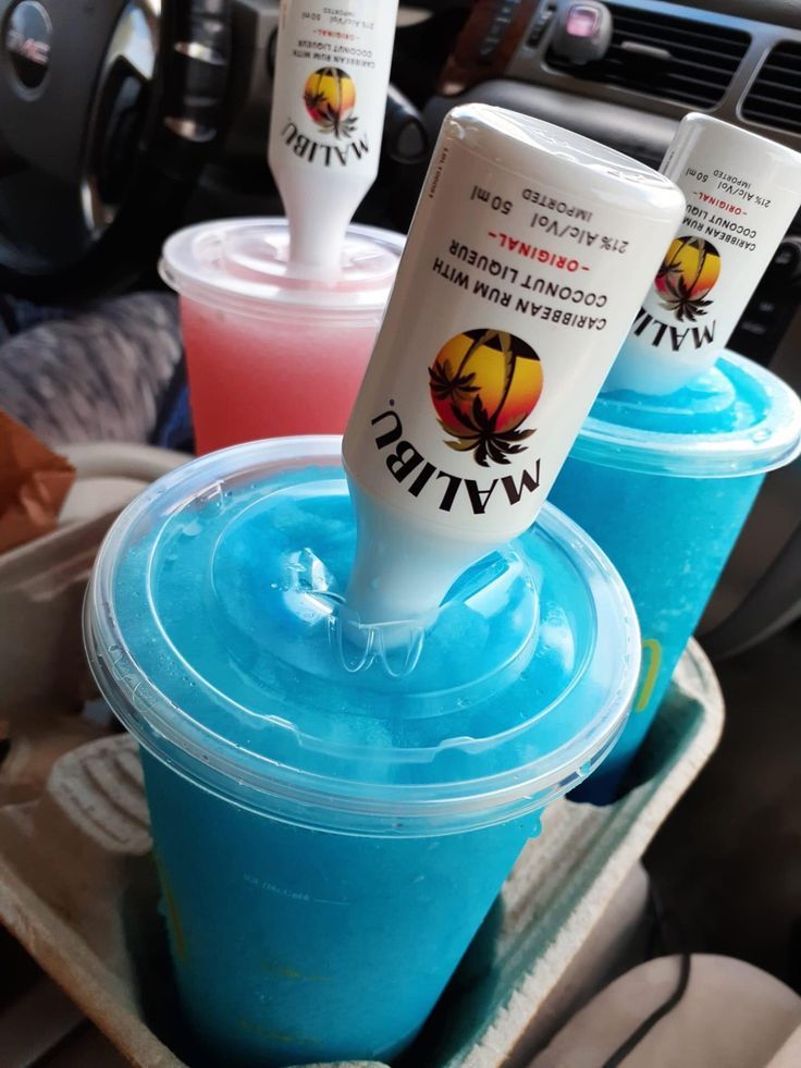 three drinks are sitting in plastic cups on the dashboard of a car, one is blue and the other is pink