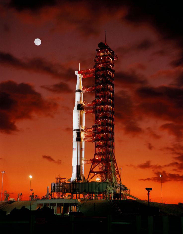 an image of a rocket on the ground at night with moon and clouds in background