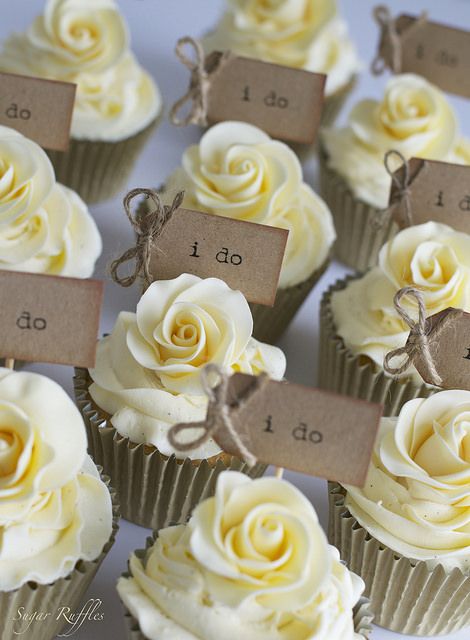 small cupcakes with white frosting and brown tags on them are arranged in rows