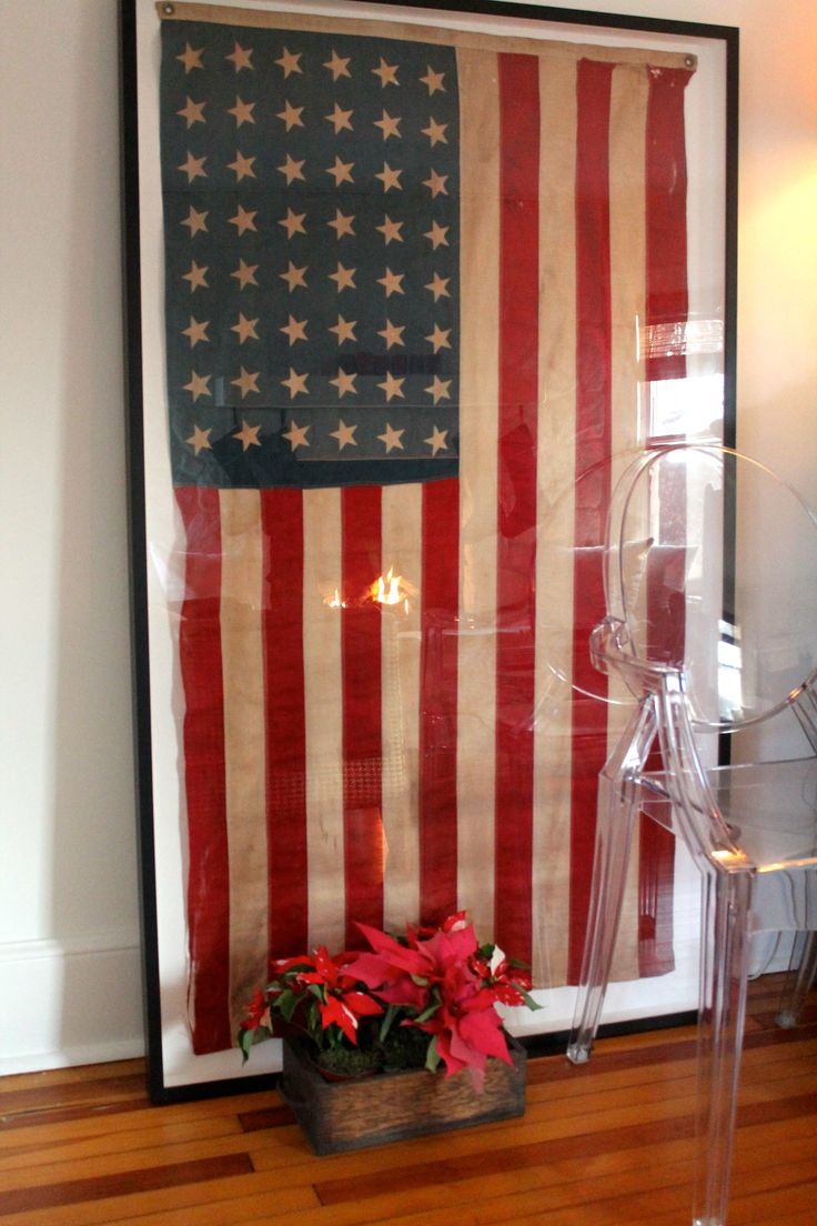 an american flag hanging on the wall behind a clear chair with poinsettis in it