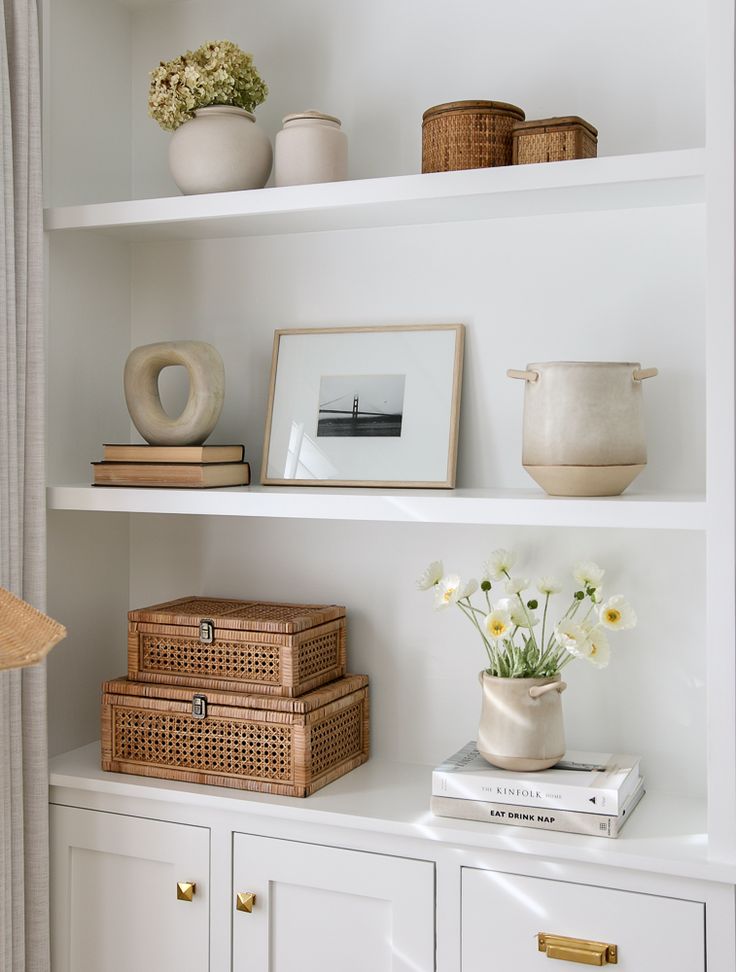 shelves with pictures and vases on them in a room that has white shelving