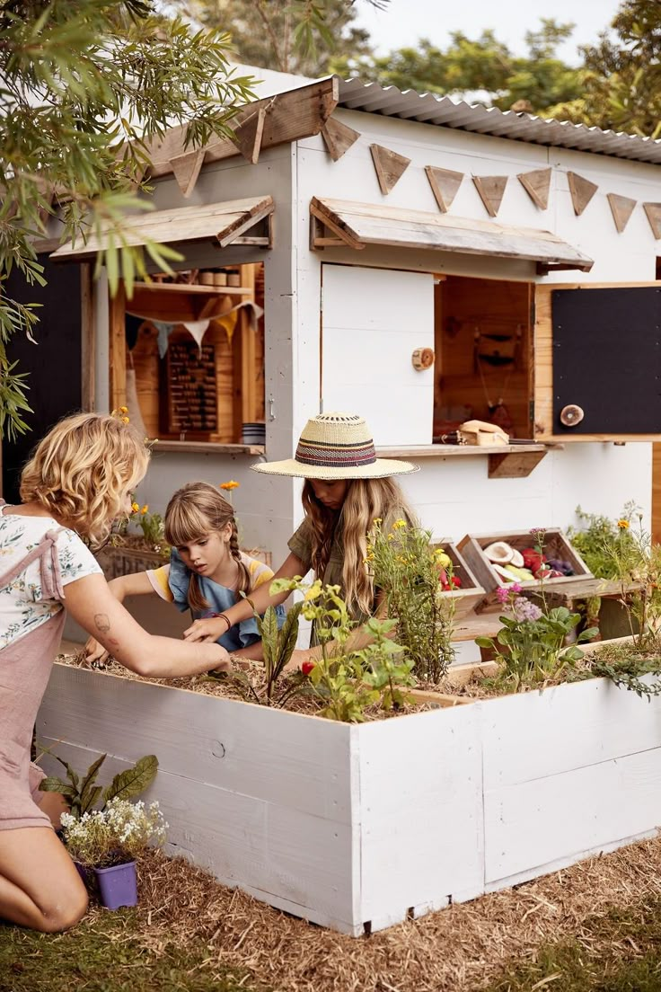 two women and a child are working in a raised garden bed that is built into the side of a house