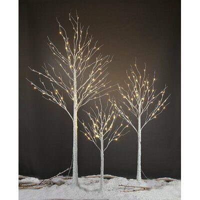 three lighted trees in the snow with no leaves on them, one is white and the other is brown