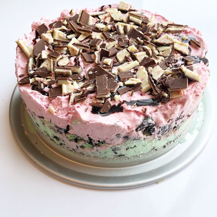 there is a cake with pink frosting and chocolate chips on the top, sitting on a silver plate