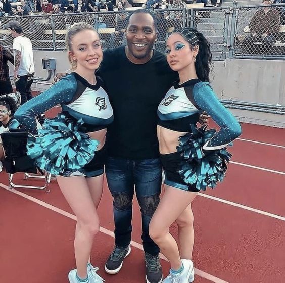 two cheerleaders are posing for a photo with their coach on the sidelines