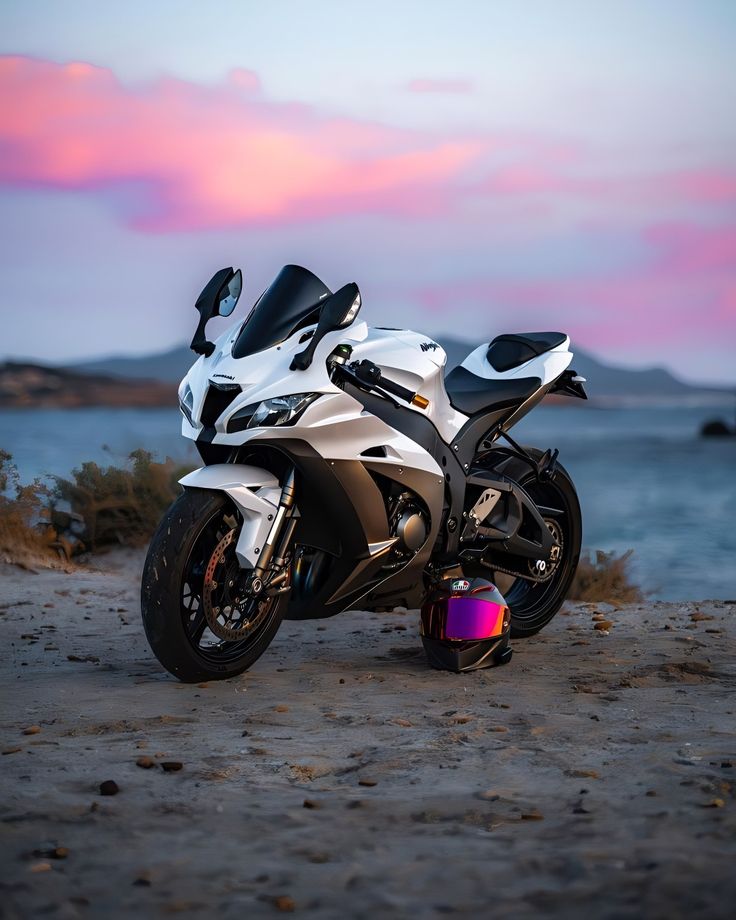 a white motorcycle parked on top of a sandy beach next to the ocean at sunset