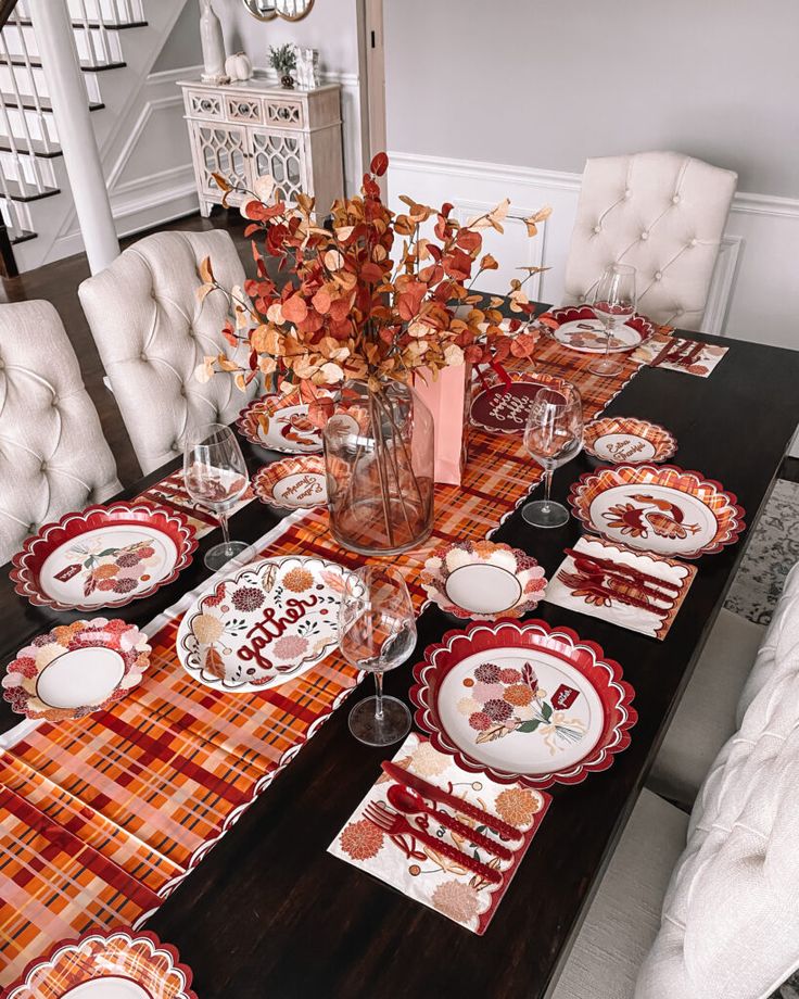 a dining room table set with plates and place settings for thanksgiving dinnerware, along with flowers in a vase