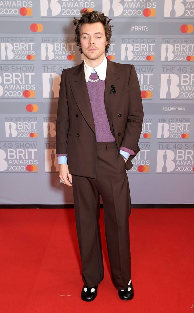 a man in a suit and tie standing on a red carpet with his hands in his pockets