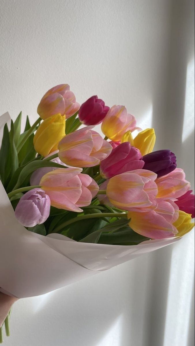 a bouquet of tulips is wrapped in white paper and held by someone's hand