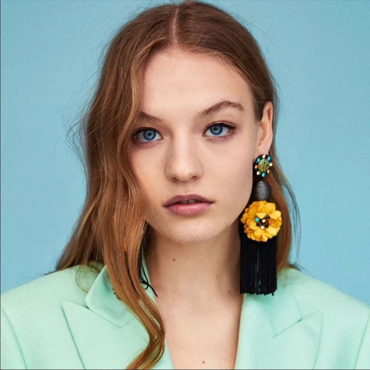 a woman with long red hair and blue eyes wearing yellow flower earrings