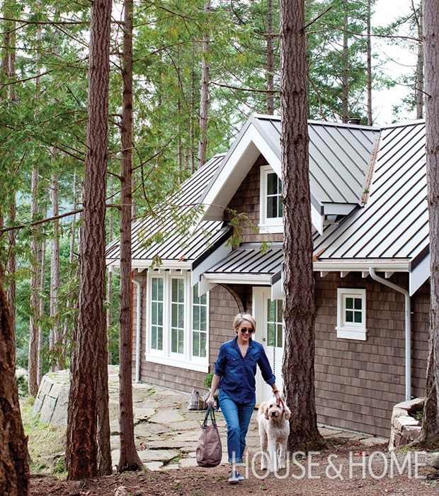 a woman walking her dog in front of a house with a metal roof and shingled windows