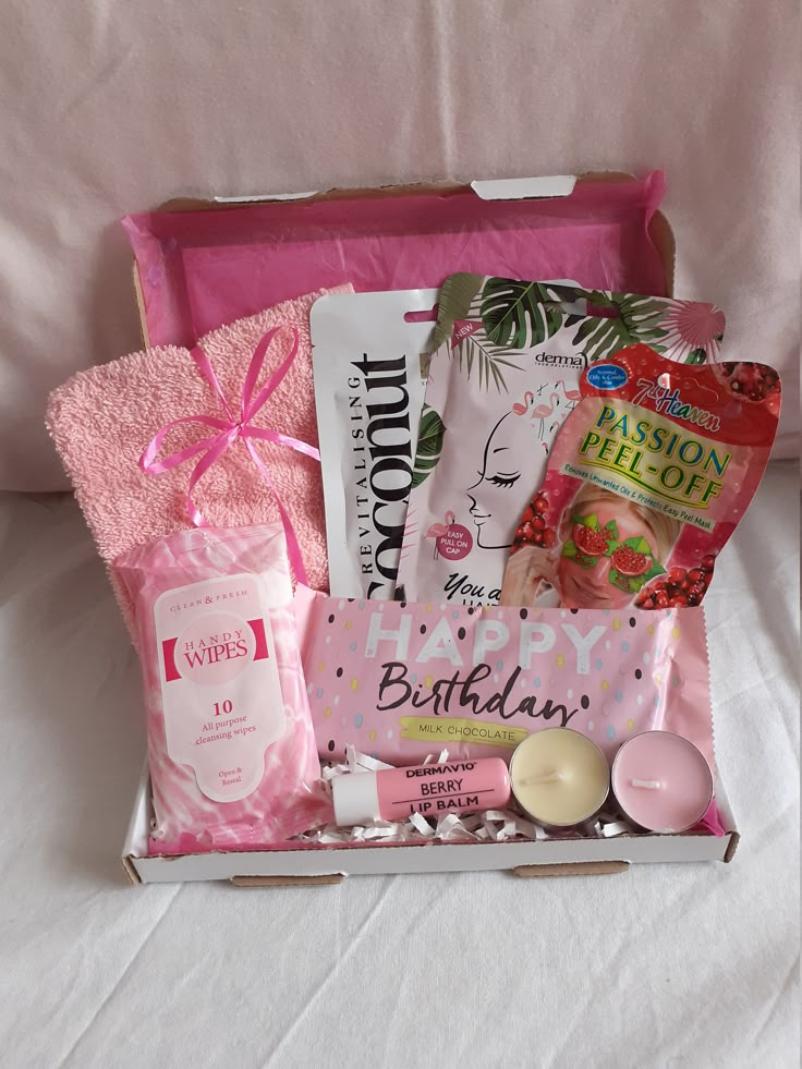 a pink gift box filled with personal care items and candles on a white bed sheet