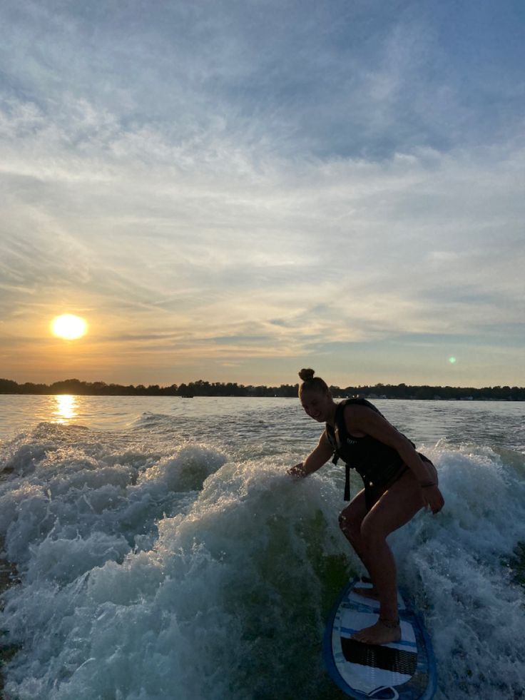 a woman riding a surfboard on top of a wave in the ocean at sunset