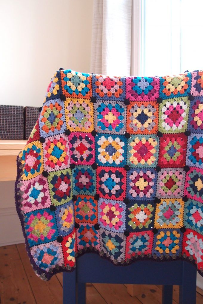 a crocheted blanket sitting on top of a blue chair next to a window