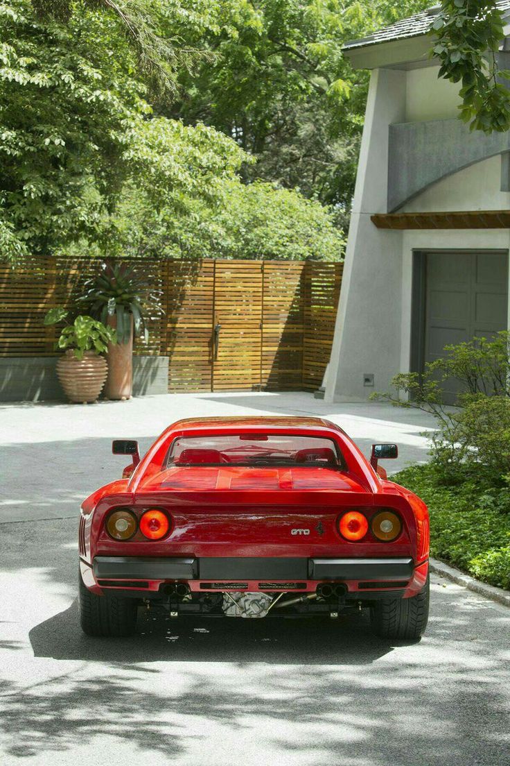 the rear end of a red sports car parked in front of a house with trees