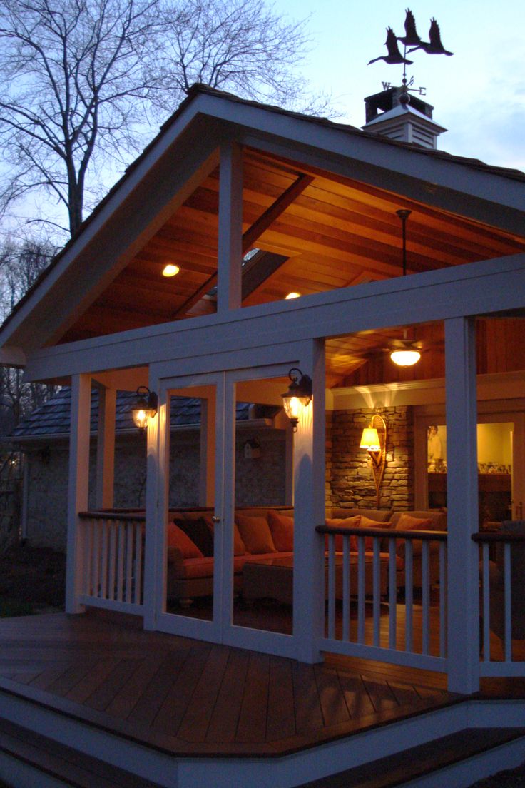 a house that is lit up at night with lights on the porch and covered patio