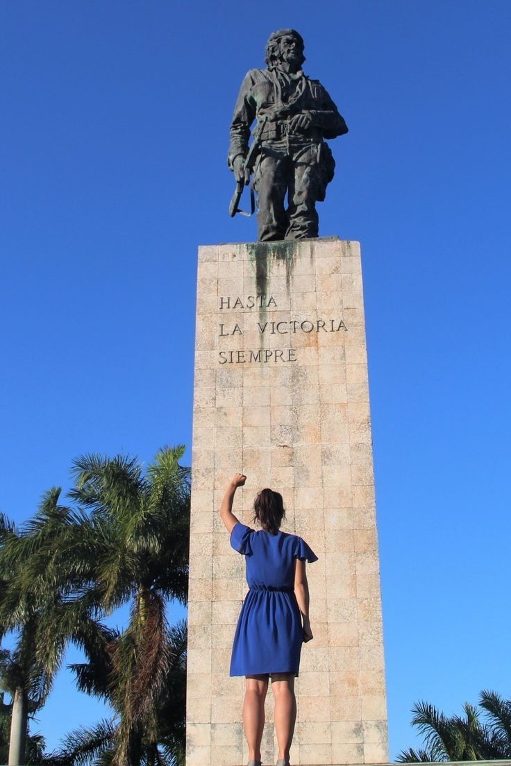 a woman in a blue dress standing next to a statue with a soldier on it