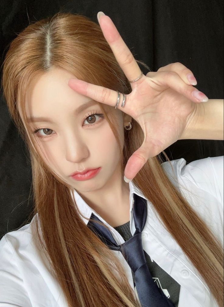 a woman with long red hair wearing a white shirt and tie making the v sign