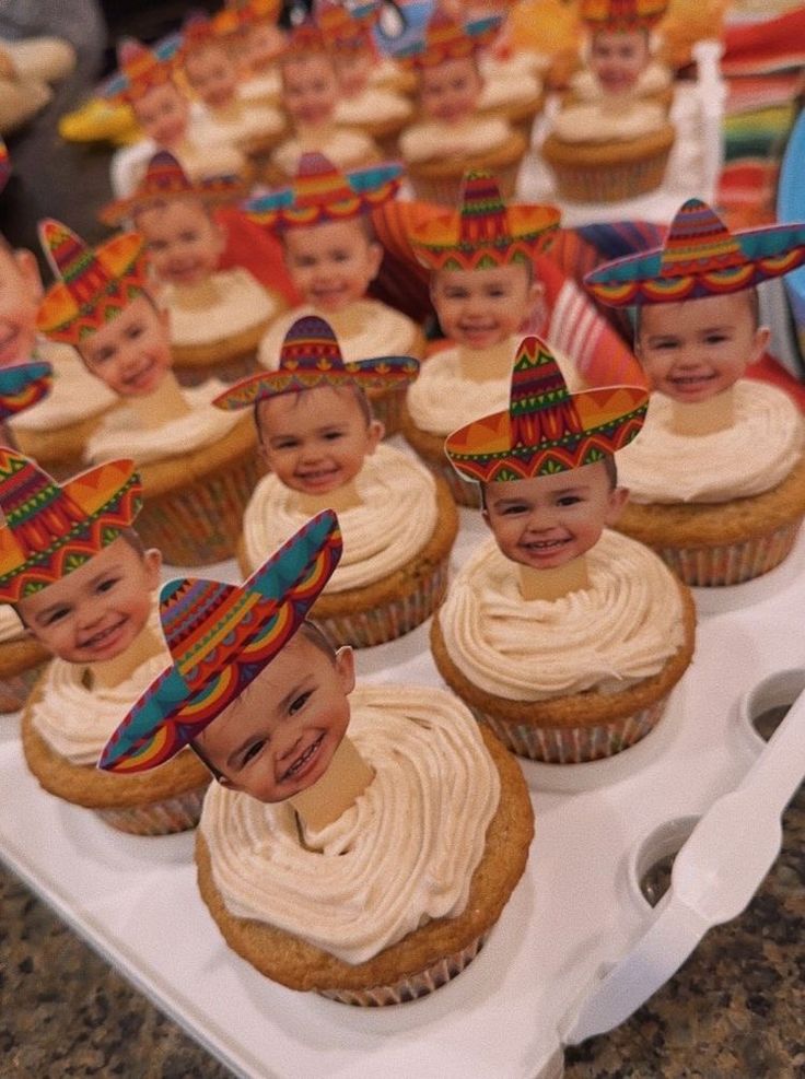 cupcakes with faces and hats on them are sitting on a tray in front of other cupcakes