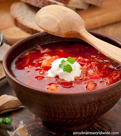 a bowl of soup with sour cream on top and bread in the backgroud