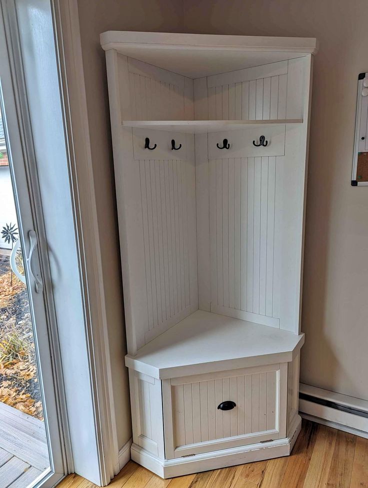 a white wooden corner shelf with three hooks on the top and two drawers below it