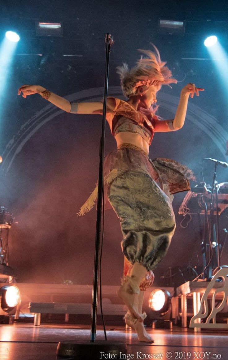 a woman is performing on stage with her legs spread out in the air while holding a microphone