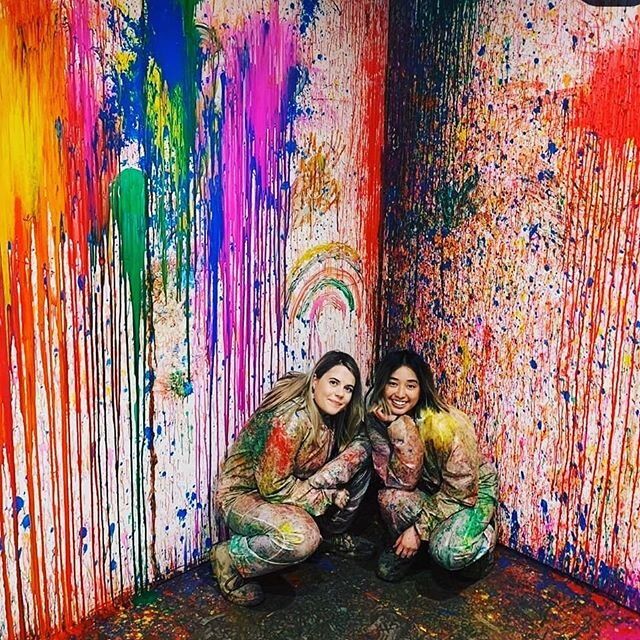 two women kneeling in front of a wall covered in paint and splattered with colors