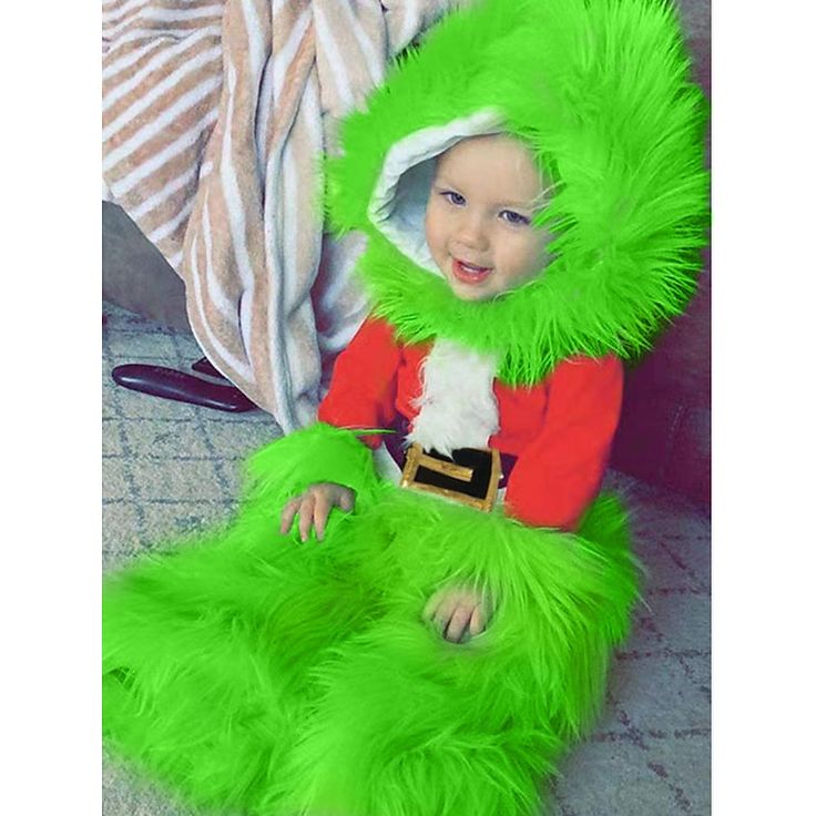 a little boy dressed in a green costume sitting on the floor with his legs crossed