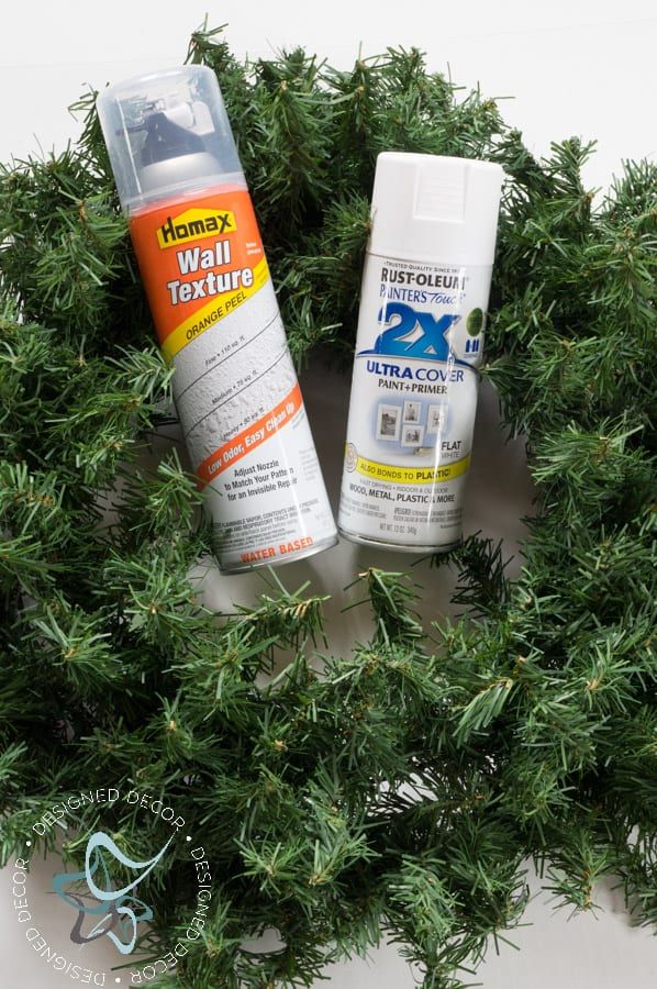 two spray paint bottles sitting on top of a green wreath with pine branches in the background