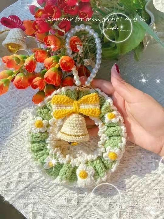 a crocheted christmas ornament with a bell on it and flowers in the background