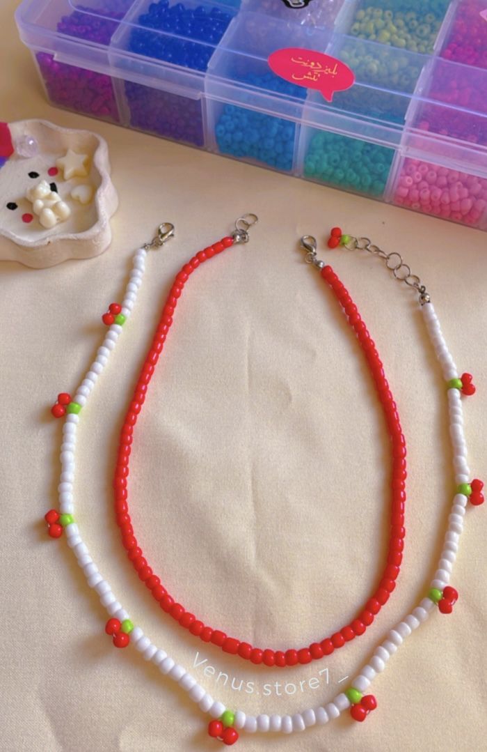 two necklaces with beads are sitting on a table next to some plastic containers and a cat figurine