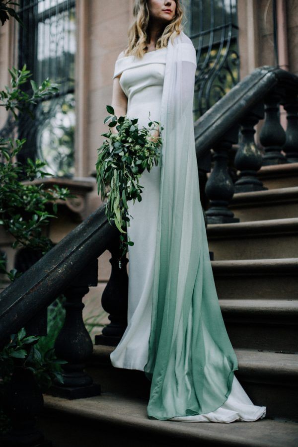 a woman in a white and green dress standing on stairs with greenery around her