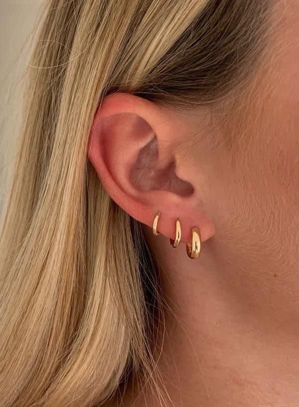 a woman with blonde hair wearing gold ear climbrs and a pair of earrings in front of her face