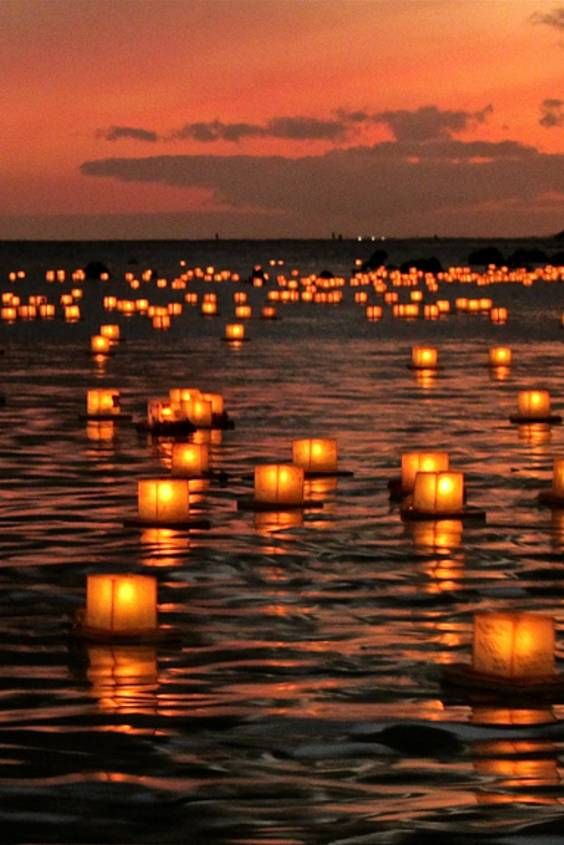 many lit candles floating in the water at sunset