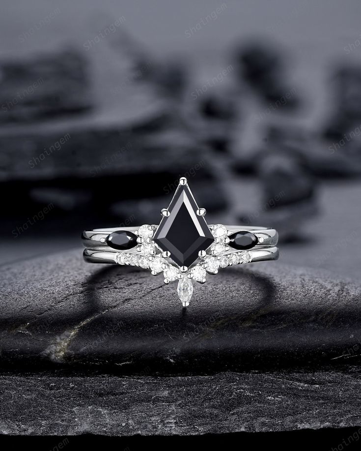 a black and white photo of an engagement ring with diamonds on the side, sitting on a rock