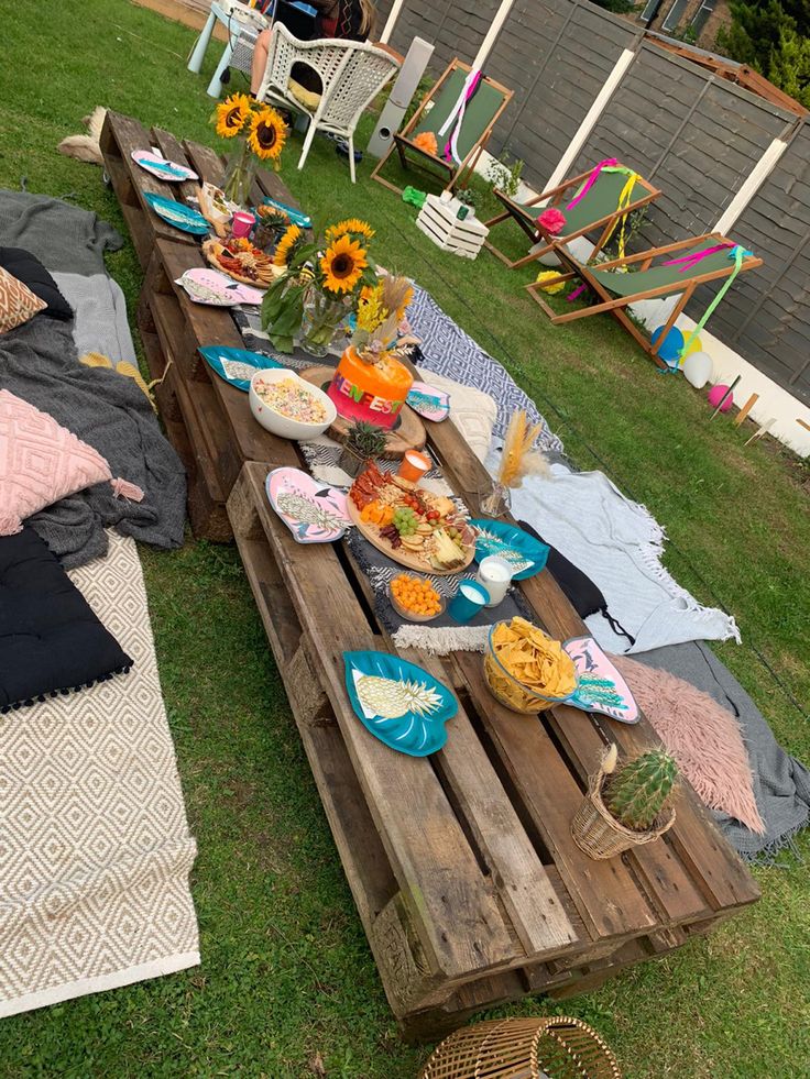 an outdoor picnic with sunflowers and plates of food on the grass next to it