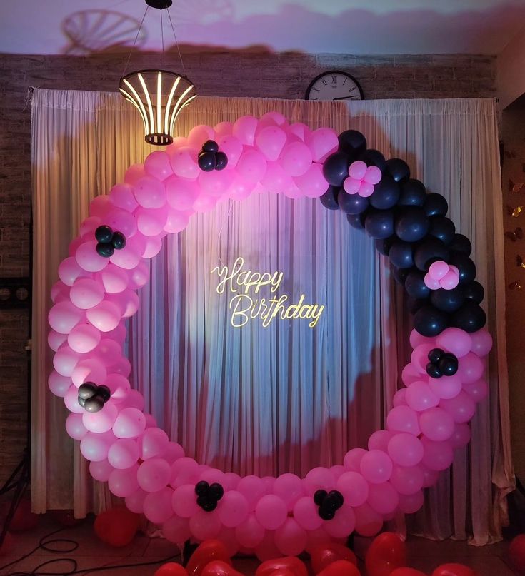 a pink and black balloon arch with happy birthday written on the front surrounded by balloons