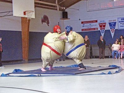 two sumo wrestlers are performing in an indoor arena while people watch from the sidelines