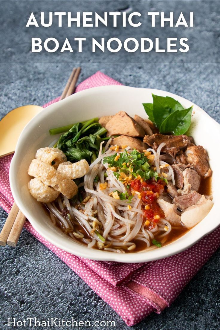 a white bowl filled with noodles and meat on top of a pink napkin next to chopsticks