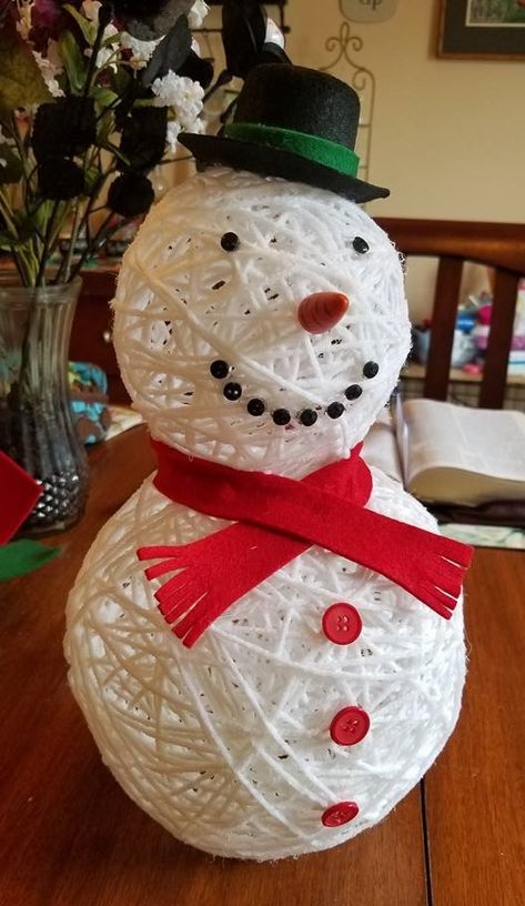 a paper mache snowman sitting on top of a wooden table next to a vase with flowers