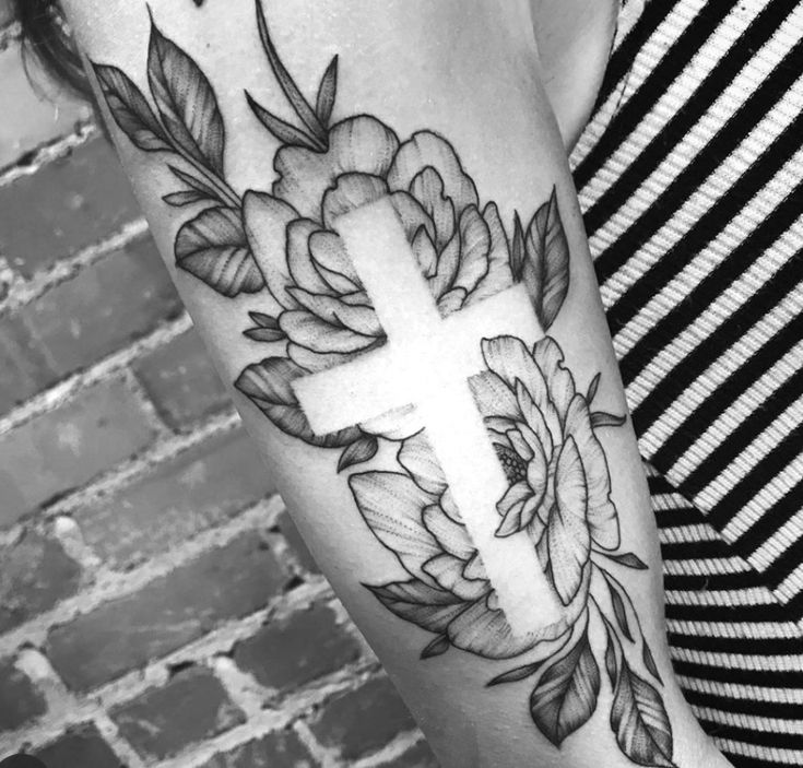 a woman's arm with a cross and flowers tattoo on the left side of her arm