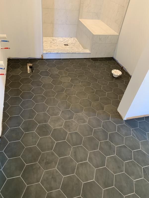 an empty bathroom with hexagonal tiles on the floor and shower stall in the background