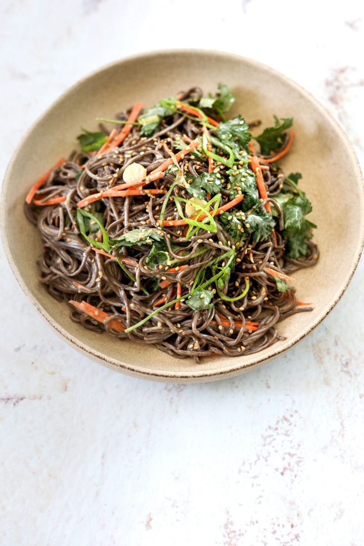 a bowl filled with noodles, carrots and greens