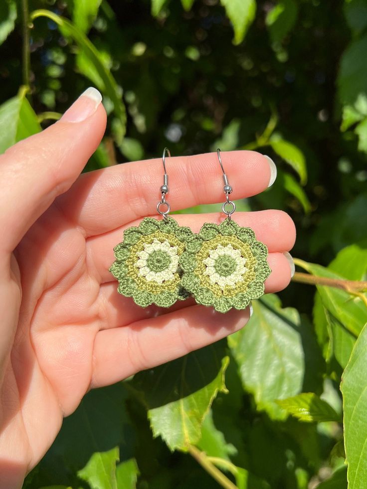 a pair of green earrings is shown in front of some leaves and bushes, with the sun shining on them