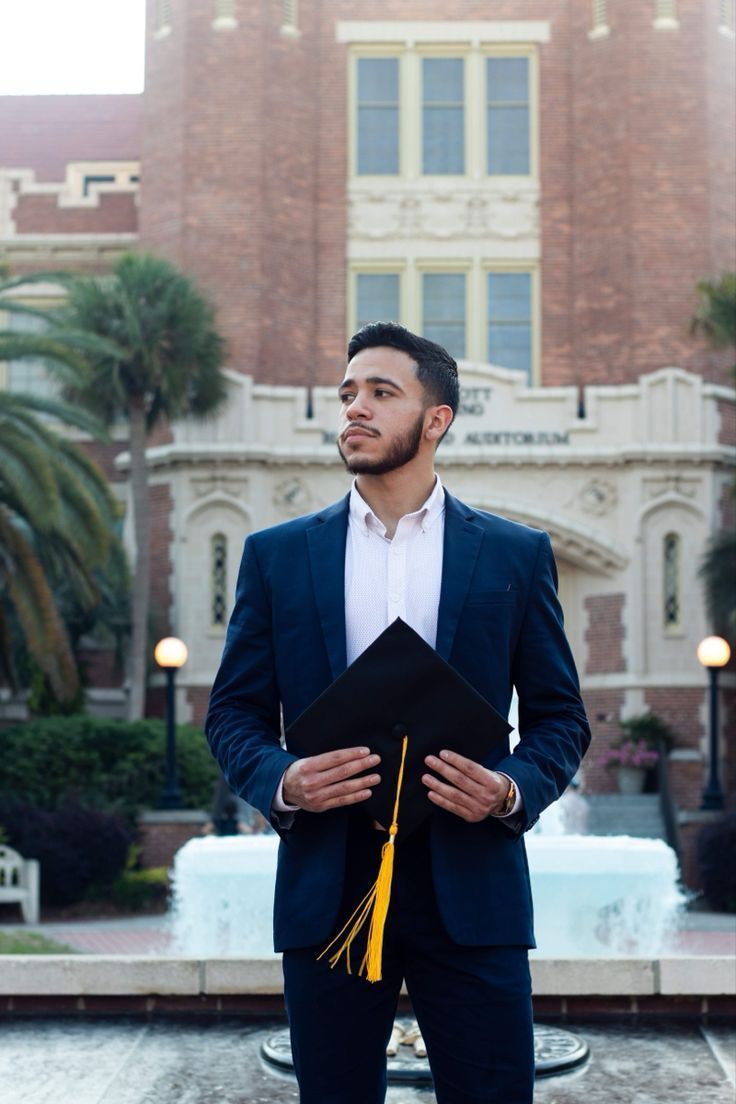 a man standing in front of a fountain wearing a suit and holding a graduation cap