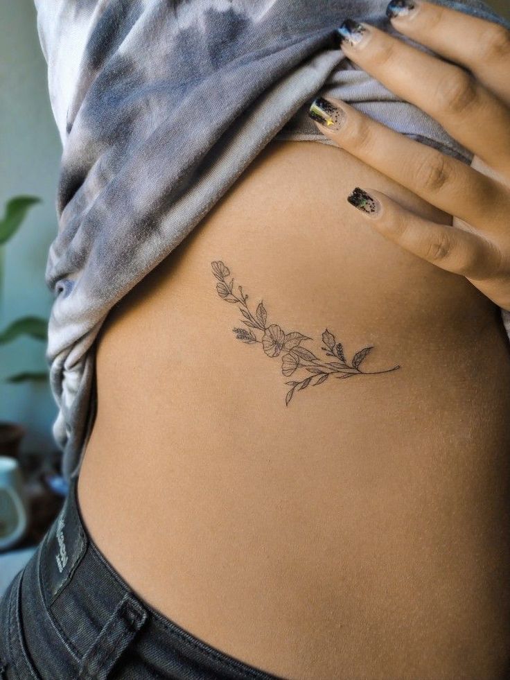 a woman's lower back tattoo with flowers on her left side ribcage