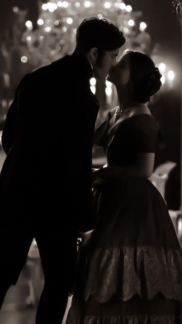 a man and woman kissing in front of a chandelier with lights behind them