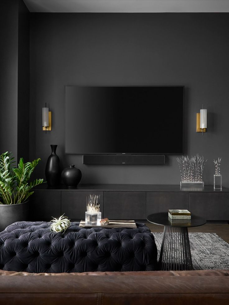 a living room with black walls and wooden flooring, a large television on the wall