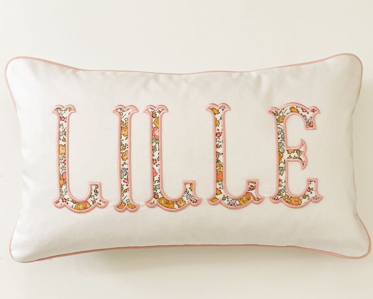 an embroidered pillow with the word lilly spelled in pink and gold glitters on it