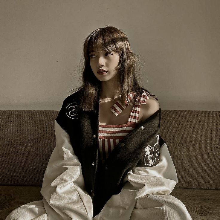 a woman sitting on top of a couch wearing a black jacket and white dress with an embellished collar